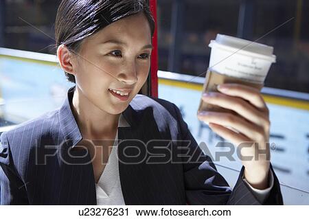 Stock Image - Young Businesswoman Riding Tram, Looking at Coffee Cup Smiling. Fotosearch