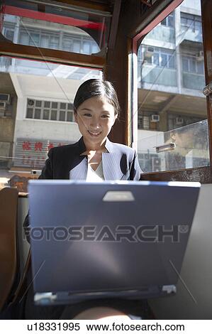 Stock Photography - Young Businesswoman Riding Tram using Laptop, Smiling. Fotosearch
