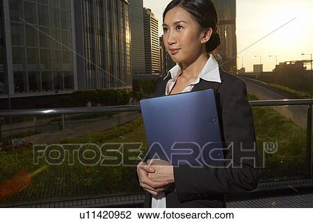 Young Businesswoman Standing in Street, Holding File, Smiling, Looking Away View Large Photo Image Stock Image - Young Businesswoman Standing in Street, Holding File, Smiling, Looking Away. Fotosearch
