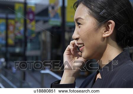 Stock Image - Young Businesswoman using mobile phone, Smiling, Close-up. Fotosearch