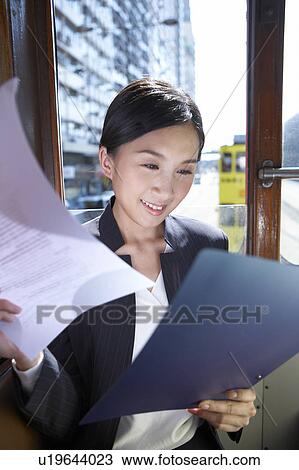 Stock Image - Young Busineswoman Riding Tram, Looking at Paperwork. Fotosearch