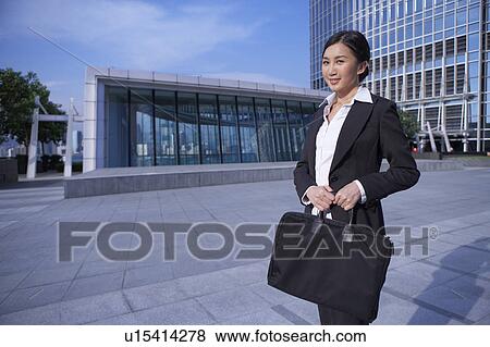 Stock Photo - Young Busineswoman Standing in Street, Carrying Briefcase. Fotosearch