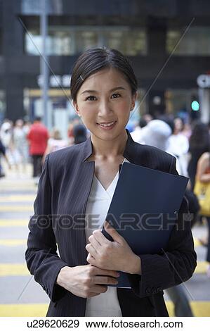 Stock Photo - Young Busineswoman Standing in Street, Holding File, Smiling. Fotosearch