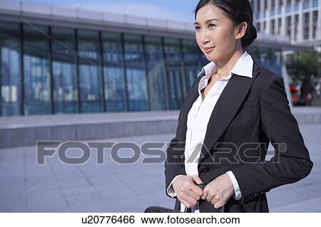 Stock Photograph - Young Busineswoman Standing in Street, Carrying Briefcase, Looking Away. Fotosearch