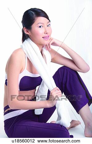 Stock Image - Young woman sitting on floor, in sporty wear. Fotosearch