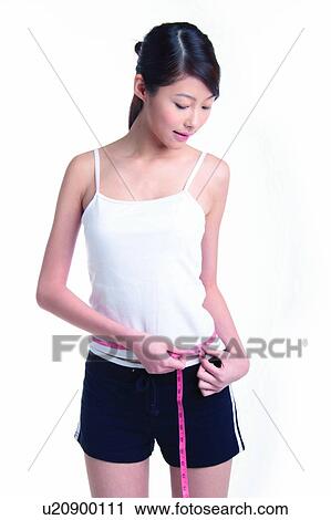 Stock Image - Young woman standing and measuring, three quarter length. Fotosearch