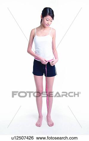 Stock Photograph - Young woman standing and measuring, full length. Fotosearch