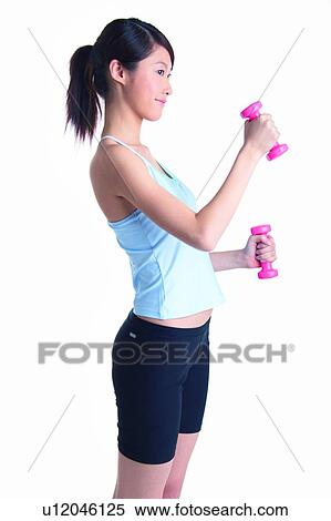Stock Photography - Young woman wearing tank top and lifting dumbbell, side view. Fotosearch