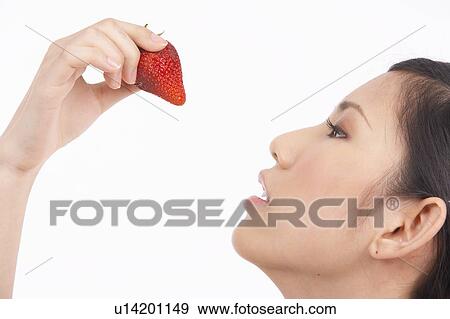 Stock Photo - Portrait of Natural Young girl eating Strawberry, side view. Fotosearch