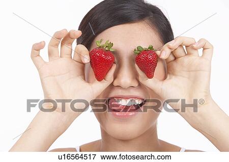 Stock Photo - Portrait of Natural Young girl holding two Strawberries on eyes. Fotosearch