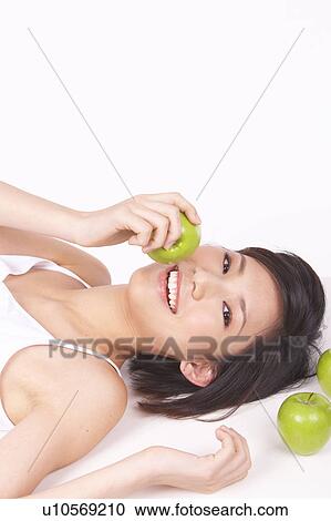 Stock Image - Portrait of Natural Young girl lying on Floor, Holding Apple. Fotosearch