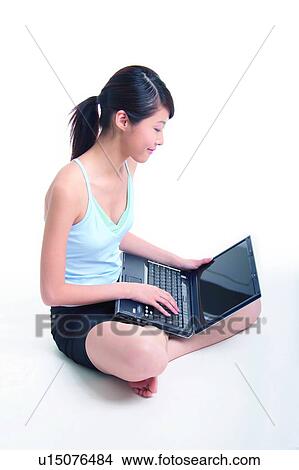 Picture - Young woman sitting and using notebook, crossed-legged. Fotosearch
