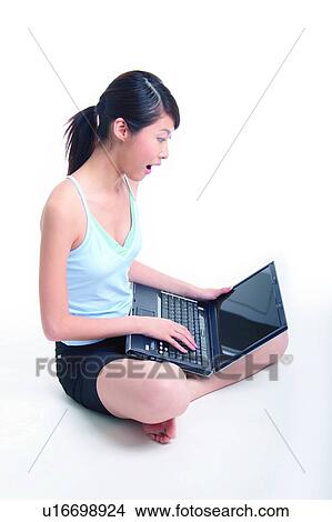 Picture - Young woman sitting and using notebook, crossed-legged. Fotosearch