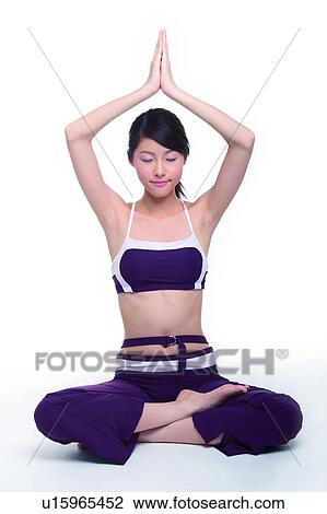 Stock Image - Young woman sitting cross-legged, doing yoga meditation exercise, eyes closed. Fotosearch