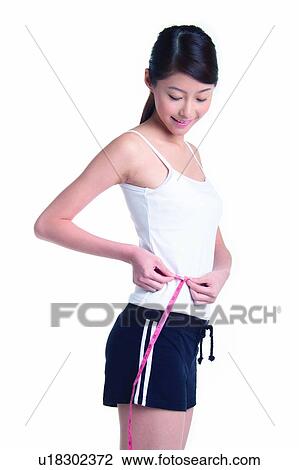 Stock Image - Young woman standing and measuring, three quarter length, side view. Fotosearch