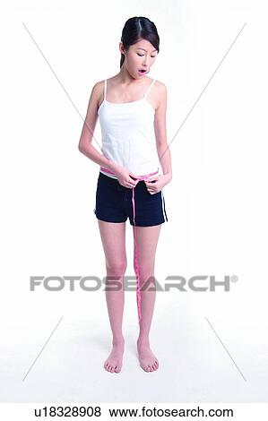 Stock Photo - Young woman standing and measuring, full length. Fotosearch