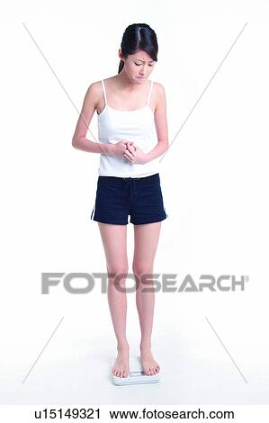 Stock Image - Young woman standing on weight scale, full length. Fotosearch