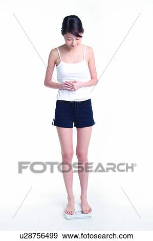 Stock Photo - Young woman standing on weight scale, full length, satisfied. Fotosearch