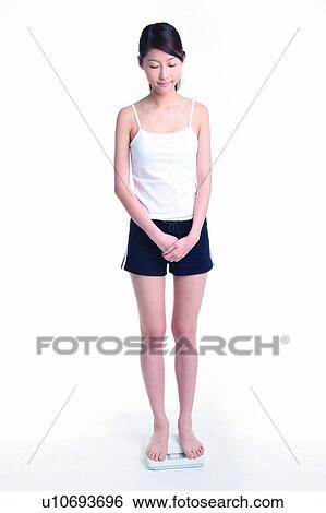 Stock Photograph - Young woman standing on weight scale, full length, eye-closed. Fotosearch