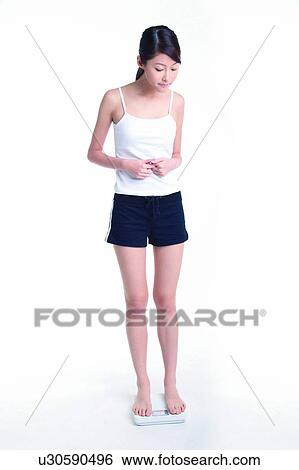 Stock Photograph - Young woman standing on weight scale, full length. Fotosearch