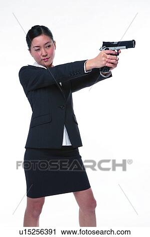 Stock Image - Young woman in business suit, holding gun, shooting. Fotosearch