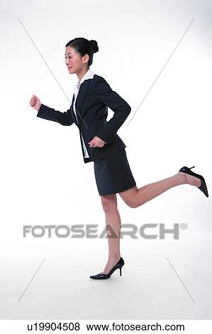 Stock Photo - Young woman in business suit, running, side view, full length. Fotosearch