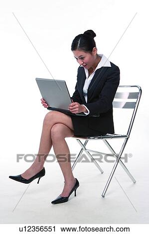 Stock Image - Young woman in business suit, sitting, using laptop, side view. Fotosearch