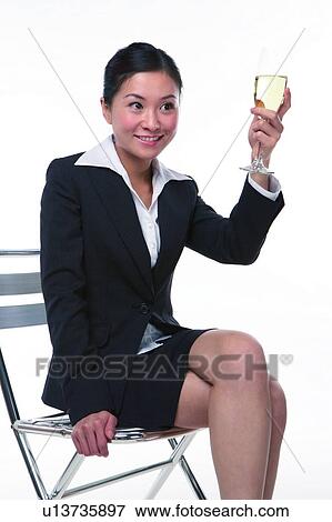 Stock Photo - Young woman in business suit, sitting, raising a glass of wine, close-up. Fotosearch