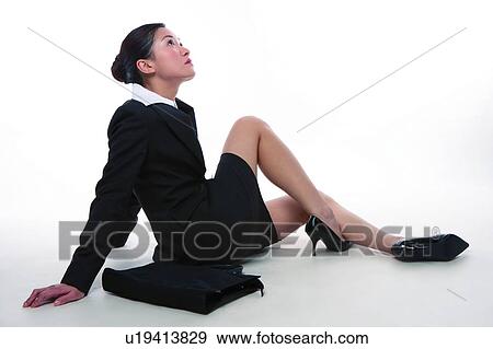 Stock Photo - Young woman in business suit, sitting on the floor, looking up. Fotosearch