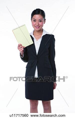 Stock Image - Young woman in business suit, standing, holding notebook with right hand. Fotosearch