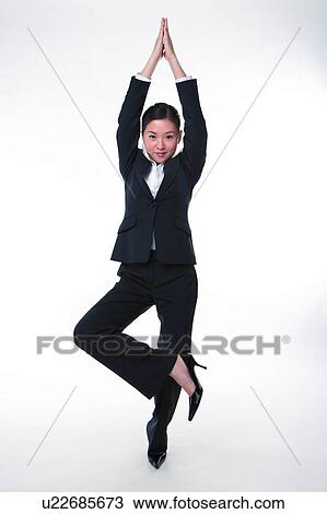 Stock Image - Young woman in business suit, standing on one leg. Fotosearch