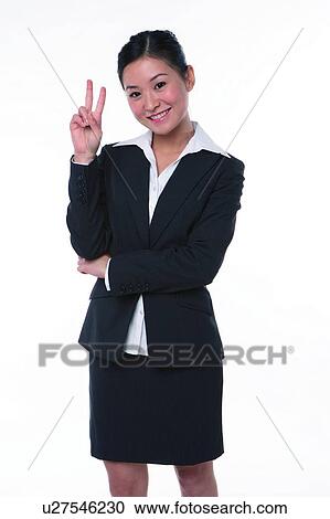 Stock Image - Young woman in business suit, standing, raising two fingers. Fotosearch