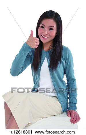 Stock Image - Young woman looking at camera, smiling with thumb up. Fotosearch