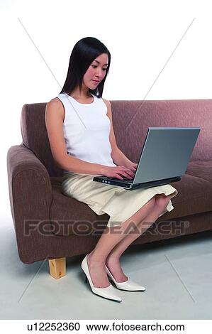 Young woman sitting on sofa and looking at laptop View Large Photo Image Stock Image - Young woman sitting on sofa and looking at laptop. Fotosearch