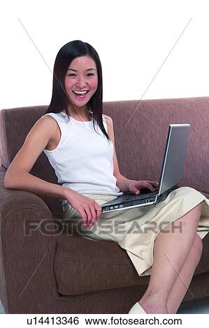 Stock Photograph - Young woman sitting on sofa and putting computers on thigh. Fotosearch