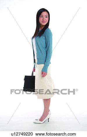 Stock Image - Young woman standing, carrying briefcase, looking back, side view. Fotosearch