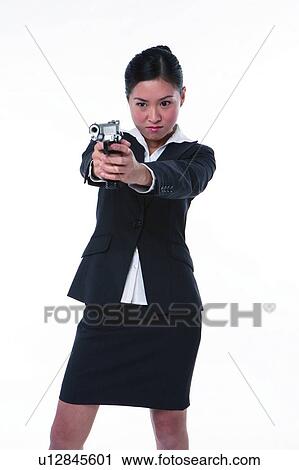 Stock Image - Young woman in business suit, holding gun, shooting, front view. Fotosearch