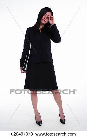 Stock Image - Young woman in business suit, holding laptop and rubbing eye. Fotosearch