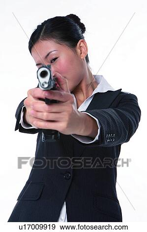 Stock Photo - Young woman in business suit, holding gun, shooting, front view, close-up. Fotosearch