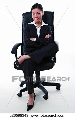 Stock Image - Young woman in business suit, sitting on armchair confidently. Fotosearch