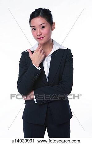 Stock Image - Young woman in business suit, standing, finger on chin. Fotosearch