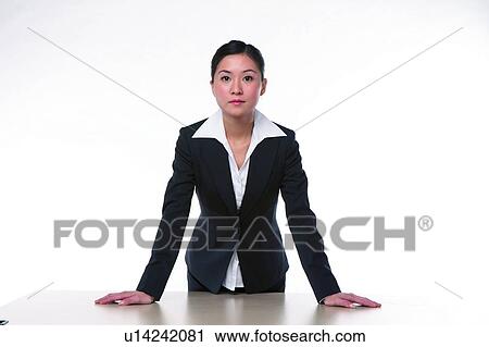 Stock Image - Young woman in business suit, standing, hands on desk. Fotosearch