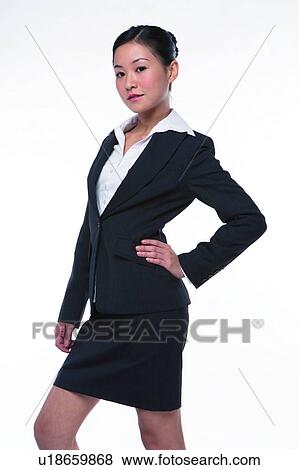 Stock Photo - Young woman in business suit, standing with one hand on waist, side view, three quarter length. Fotosearch