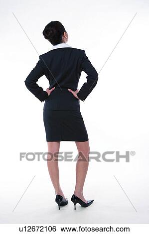 Stock Photograph - Young woman in business suit, standing with hands on waist, rear view, full length. Fotosearch