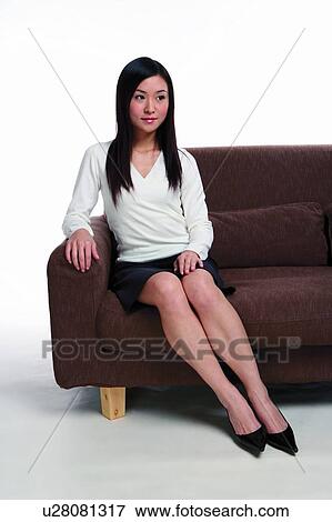 Young woman sitting on sofa, looking at away, smiling View Large Photo Image Stock Photo - Young woman sitting on sofa, looking at away, smiling. Fotosearch