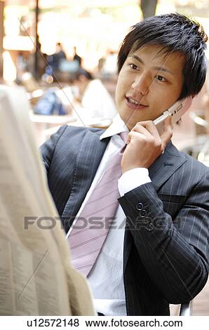 Stock Photo - Businessman talking with a cell phone and watching a newspaper. Fotosearch