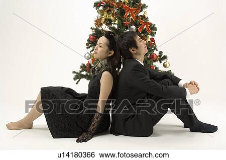 Stock Photograph - Couple sitting next to Christmas tree. Fotosearch
