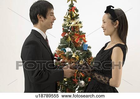 Couple standing next to Christmas tree View Large Photo Image Stock Photography - Couple standing next to Christmas tree. Fotosearch