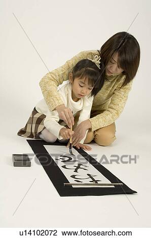 Stock Image - Mother and daughter writing letters with ink brush. Fotosearch