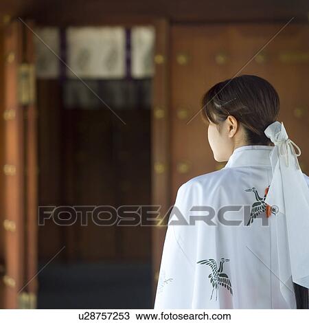 Stock Image - Female attendant standing at shrine. Fotosearch